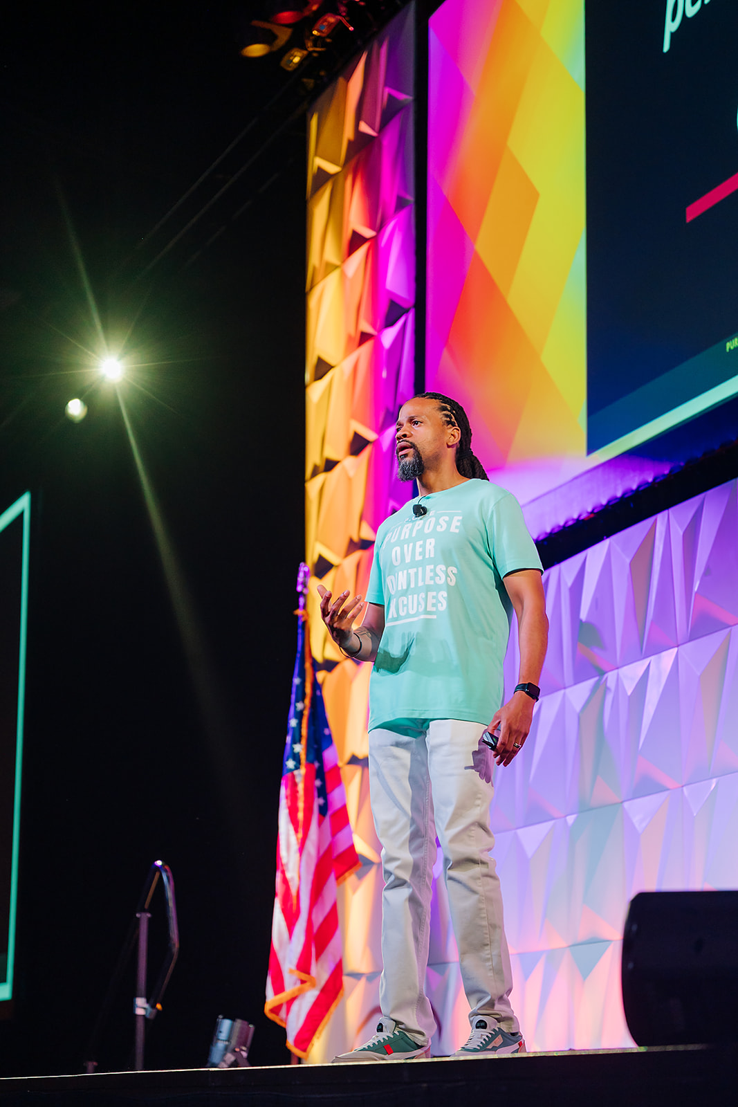 Keynote speaker addressing a large conference audience on a brightly lit stage with a colorful LED backdrop