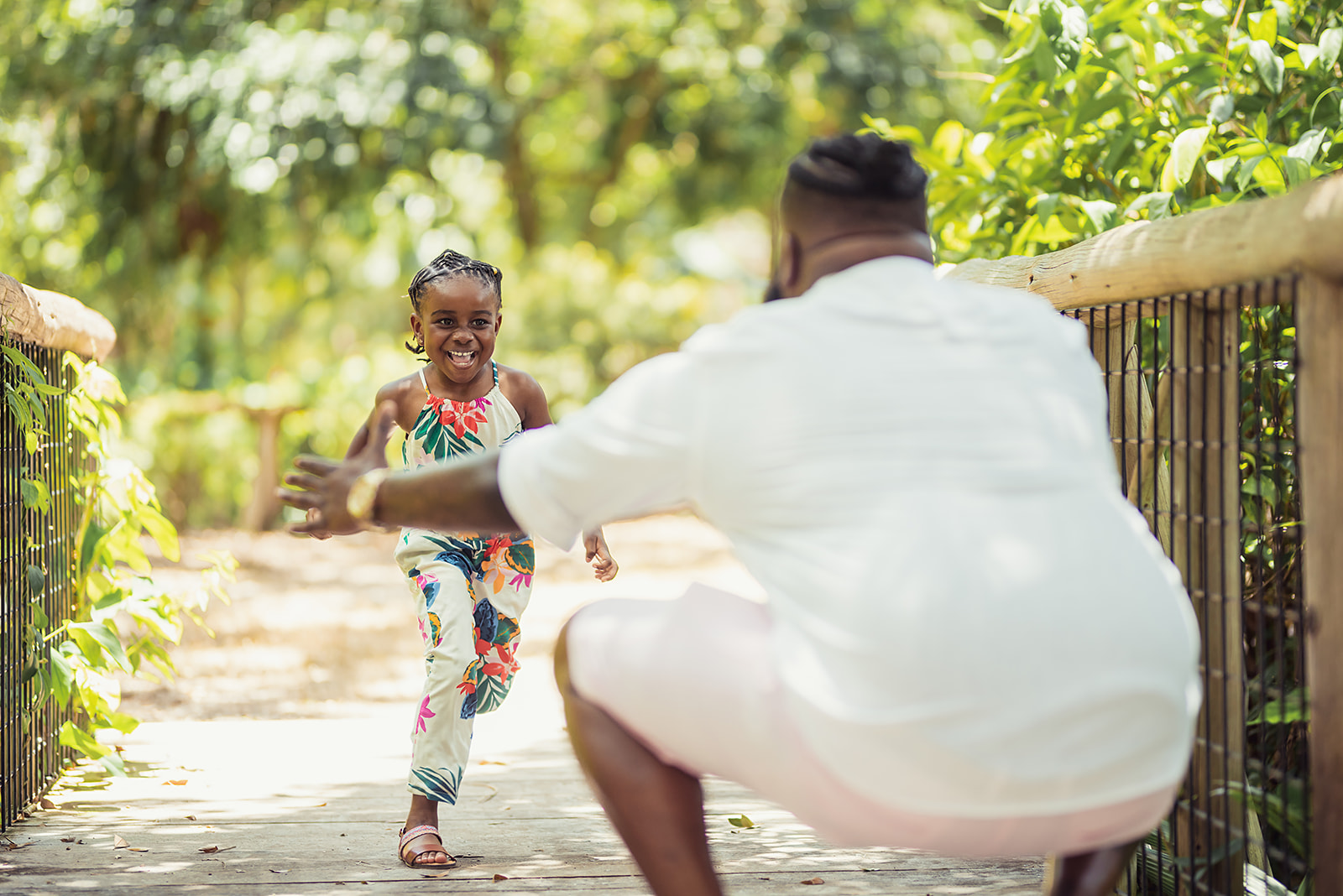 Young girl running into her dad's arms on a sunlit garden bridge