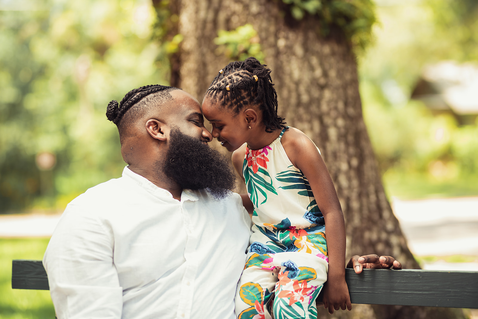 Father and daughter sharing a tender forehead kiss on a park bench during a Father's Day photoshoot